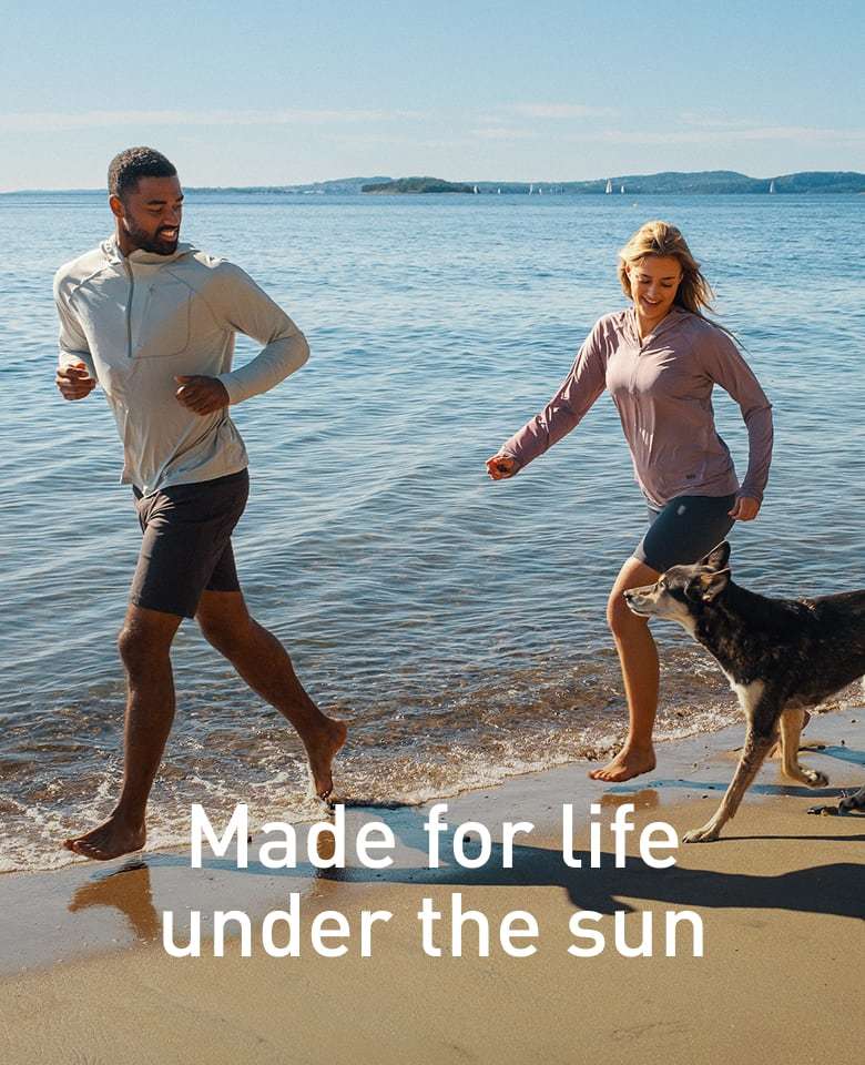 Man and woman with dog on the beach, wearing Helly Hansen sun protective clothing