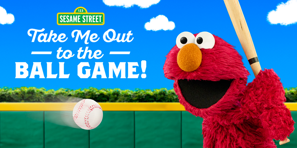 Elmo, the character from Sesame Street, smiles broadly while holding a baseball bat and takes a swing at a baseball. In the background, there’s a bright blue sky and baseball field. The title reads, “Take me out to the ball game!” below a Sesame Street logo.