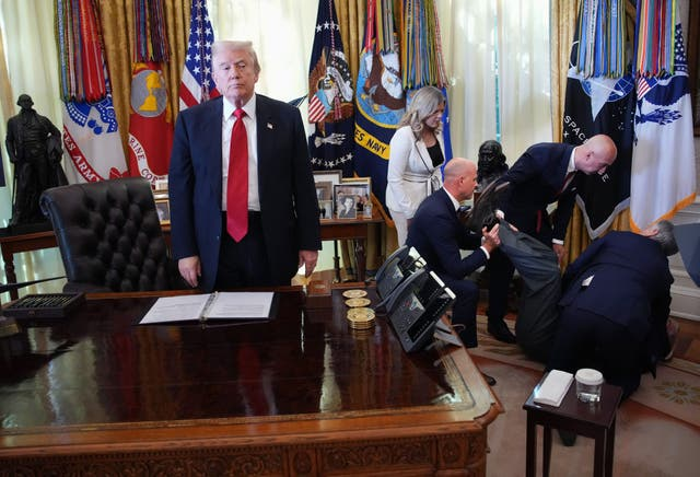 Donald Trump stands in the Oval Office while people tend to a man who fainted
