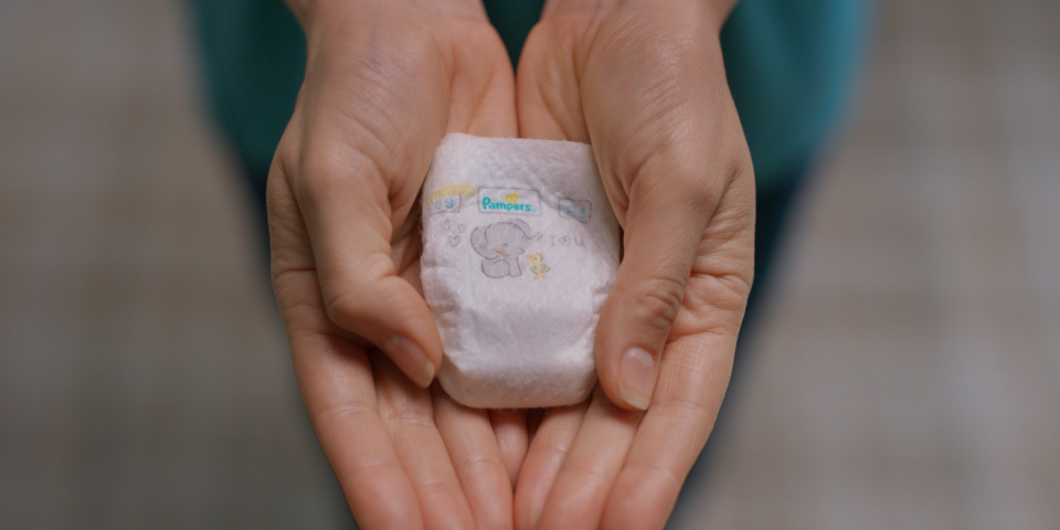 Image of a Pampers Pxxs diaper which fits snugly into the palms of a parent’s outstretched hands.