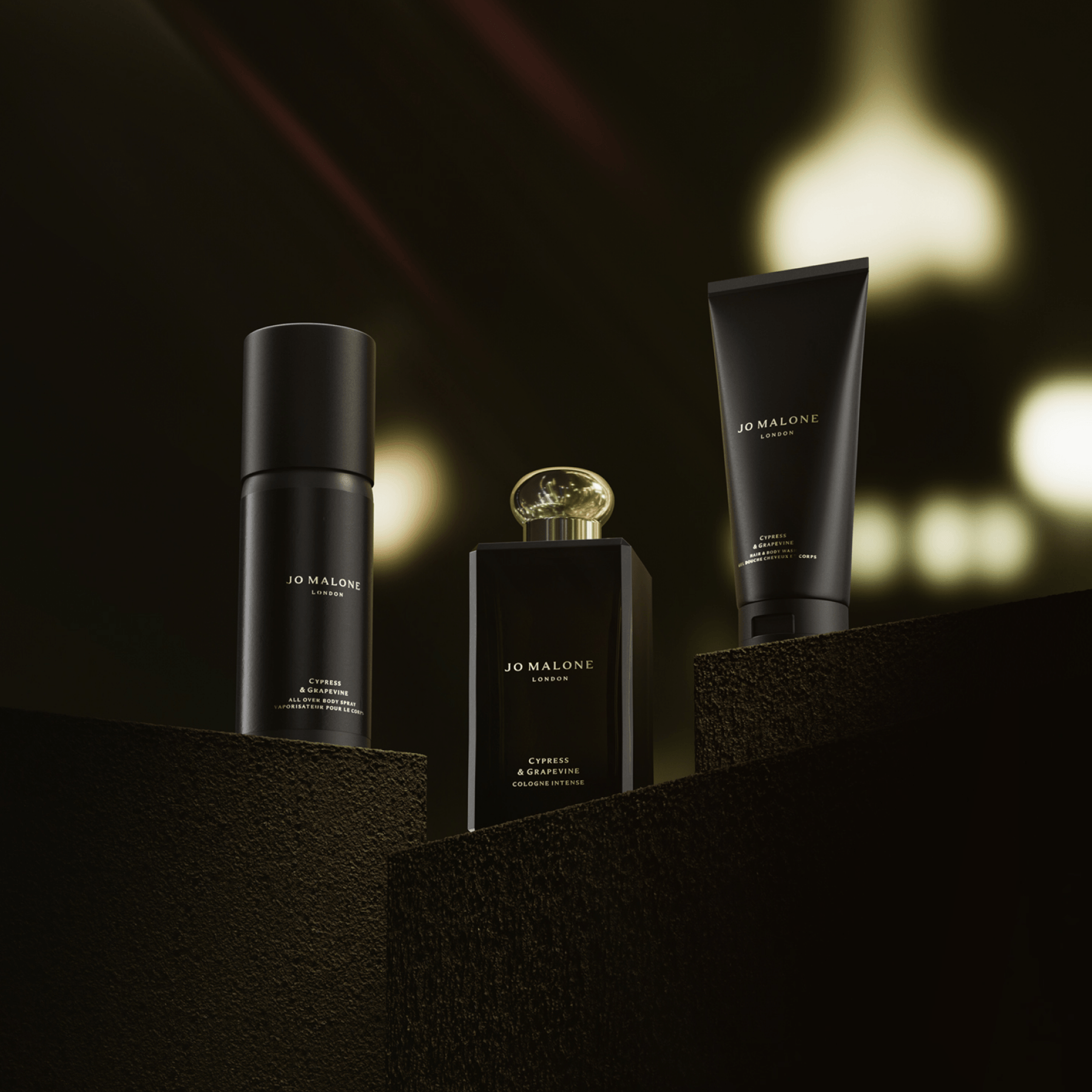 Cypress & Grapevine grooming essentials arranged on textured, dark brown platforms, against a softly blurred, warm bokeh background.