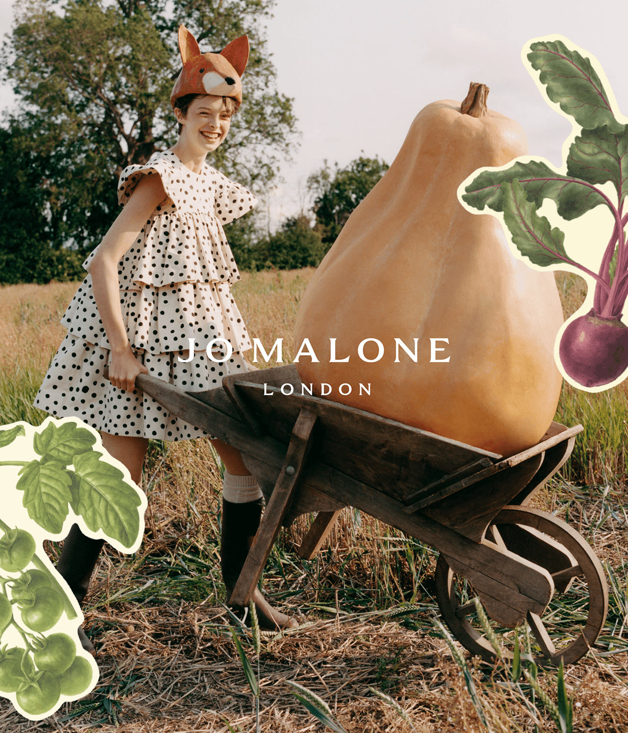 Whimsical scene of a woman in a polka-dot dress and fox hat, pushing a wooden wheelbarrow with a giant butternut squash in a rural environment, surrounded by illustrations of green tomatoes and a purple beetroot with leafy greens, and Jo Malone London logo overlaying in the centre.