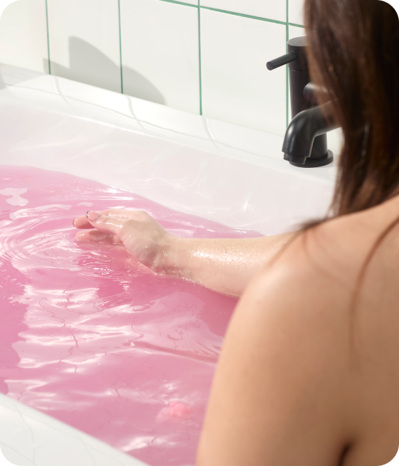 image: A person relaxing in a bath tub in pink waters of the Sex Bomb Bath Bomb