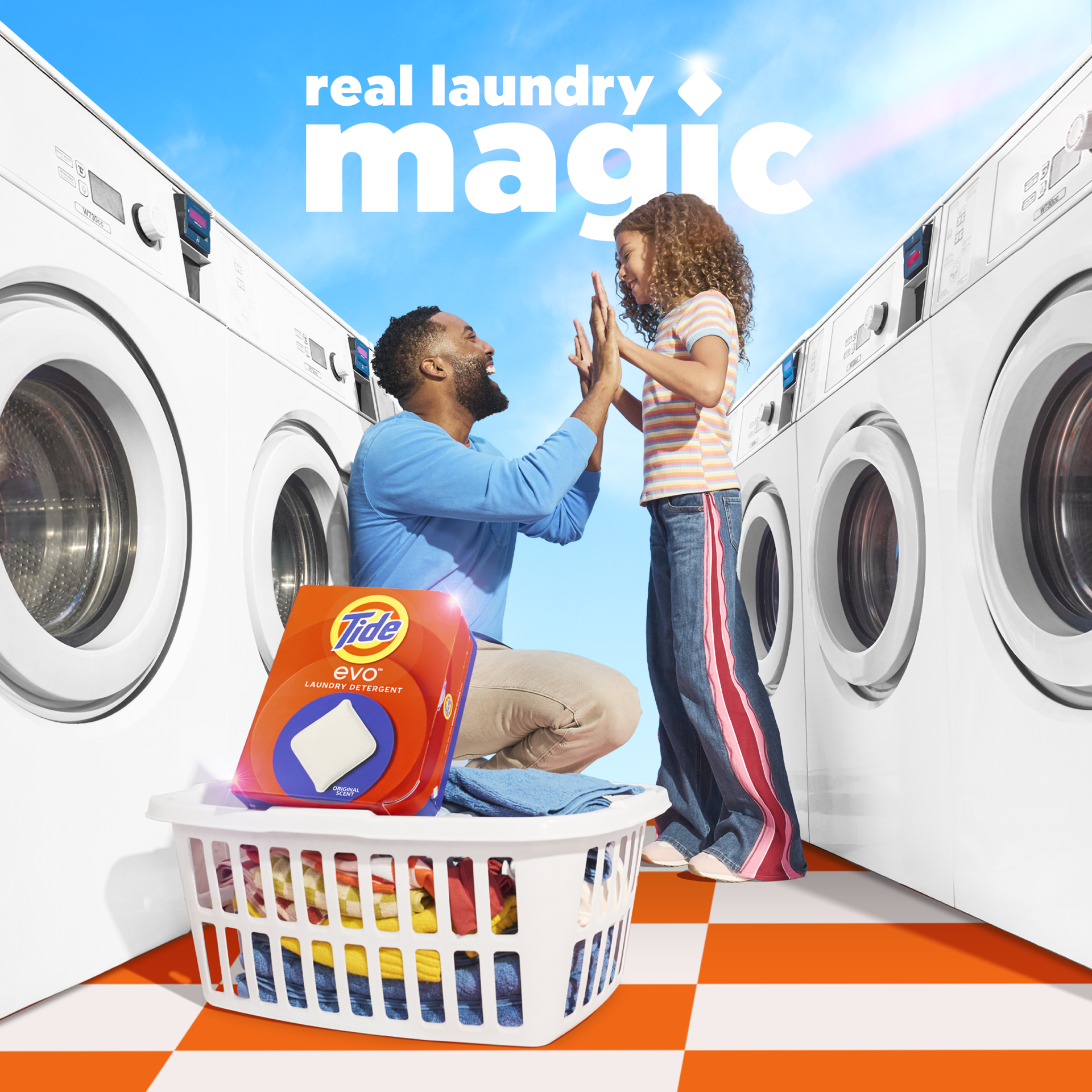 A bright laundromat scene shows an adult kneeling beside a child as the two high-five between rows of washing machines. A Tide evo laundry tile package sits on top of a full laundry basket in the foreground. Text reads: “real laundry magic.”