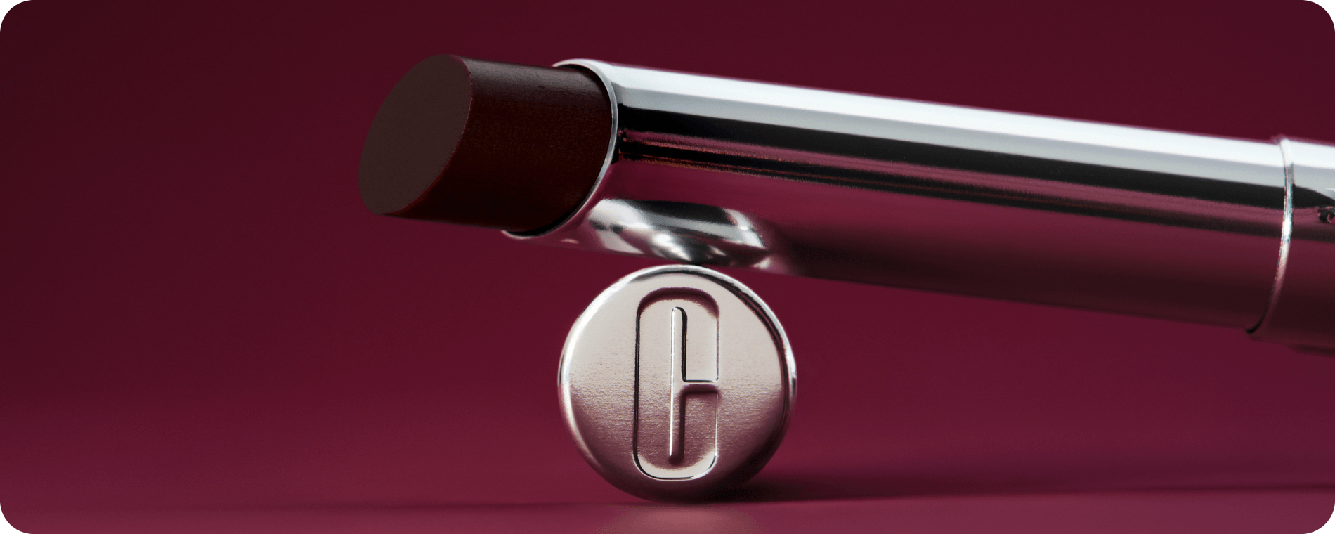 Close up of Clinique's iconic Almost Lipstick in Black Honey in front of a burgandy gradient background