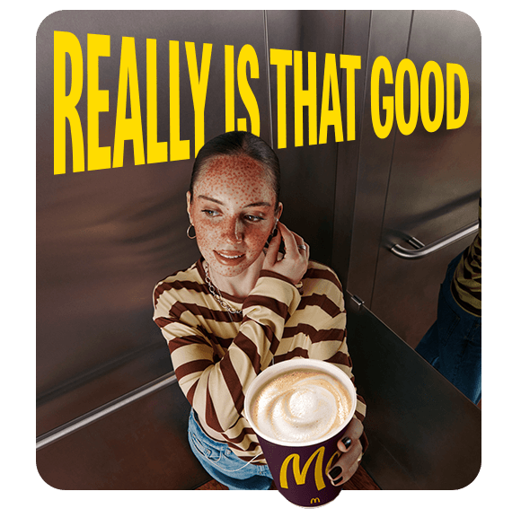 A woman standing in an elevator, holding a McCafe coffee. Text alongside her reads 'Really is that good'.